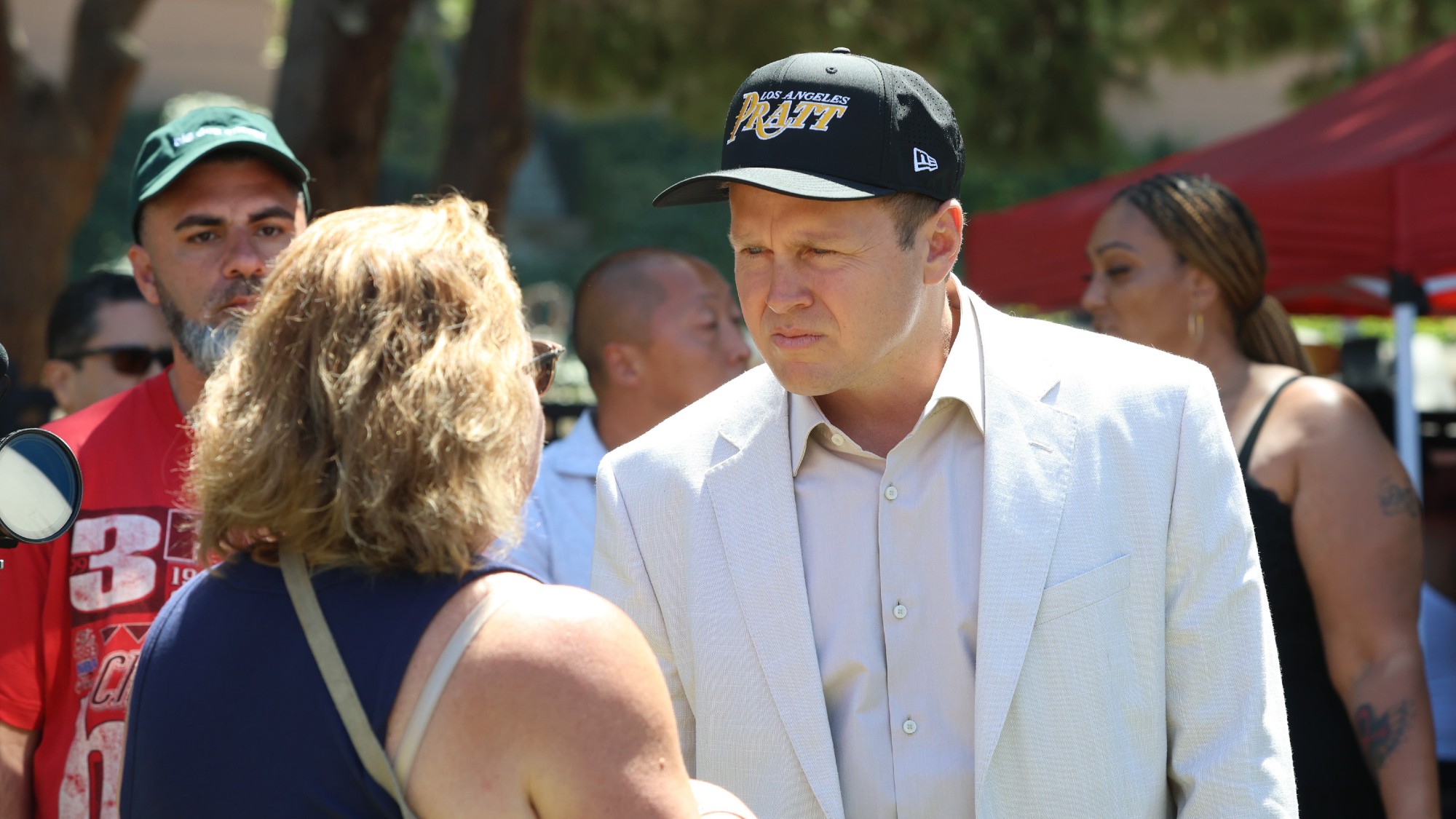 spencer pratt, dressed in a white blazer with a black hat with his last name on it greets a supporter
