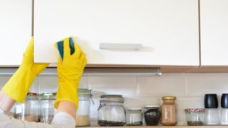woman using sponge to spot clean kitchen cabinets