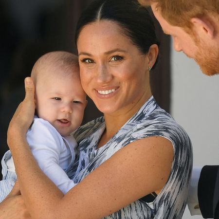 Meghan Markle wears a blue and white dress and cradles a young Prince Archie