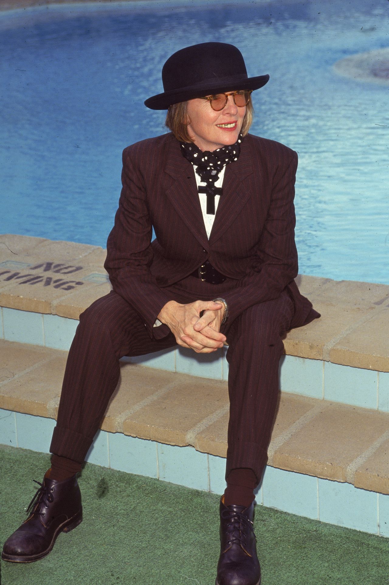 Diane Keaton's style evolution: Diane Keaton as she sits near a swimming pool, 1996. She wears a purple &amp; black striped suit, bowler hat, and, around her neck, wears a large black crucifix. (Photo by Bob Grant/Fotos International/Getty Images)