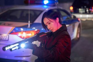 a woman (Lee Jung-hyun as Choi Jun-kyung) aims a shotgun while standing by a police car, in 'parasyte the grey'