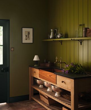 utility room with dark green panelled walls, wooden unit with sink and rustic decor