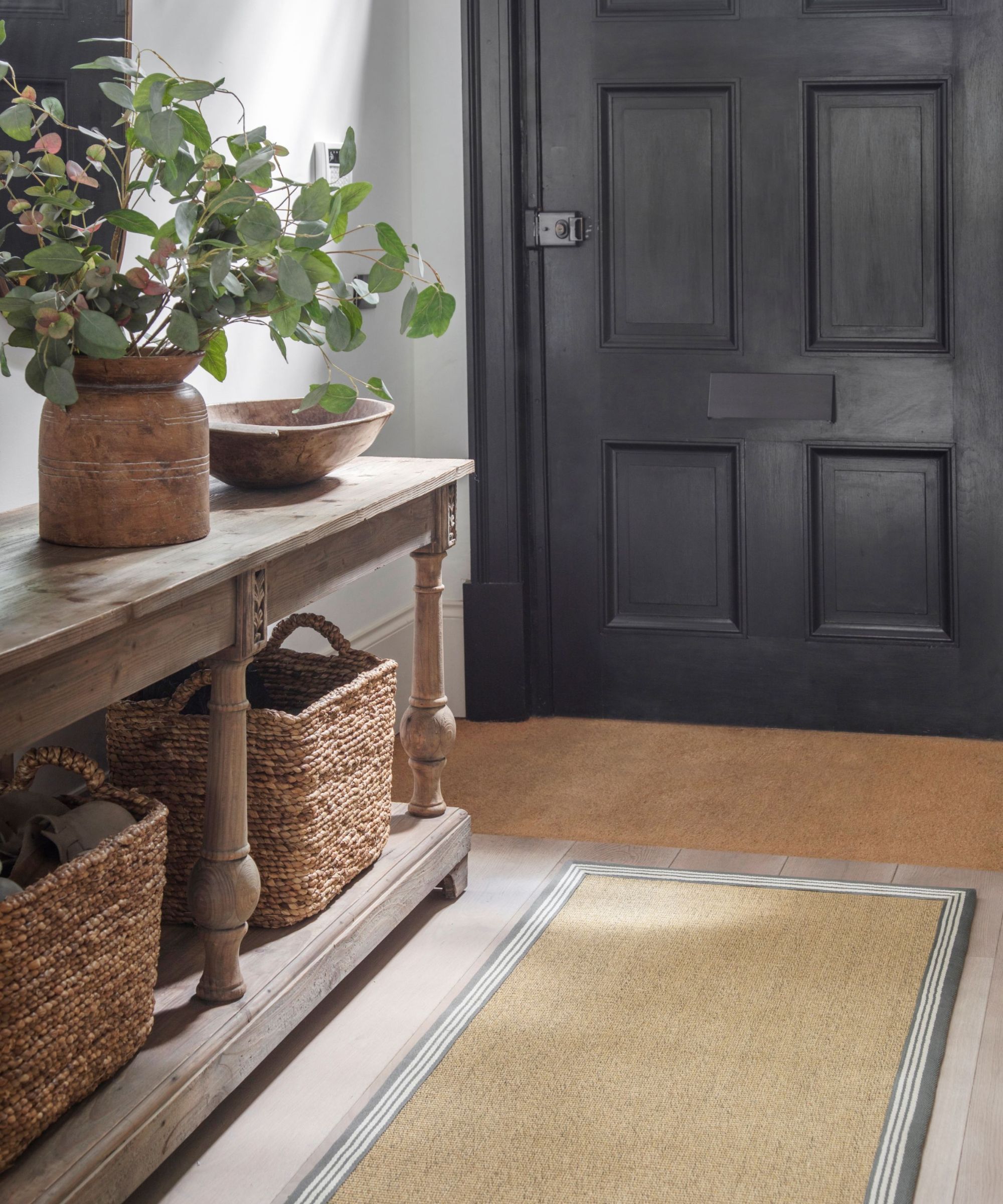 Characterful hallway with a black panelled front door, rustic wood console, woven storage baskets and a smart jute-style runner with striped border.