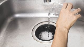 Vinegar being tipped into a drain on top of baking soda