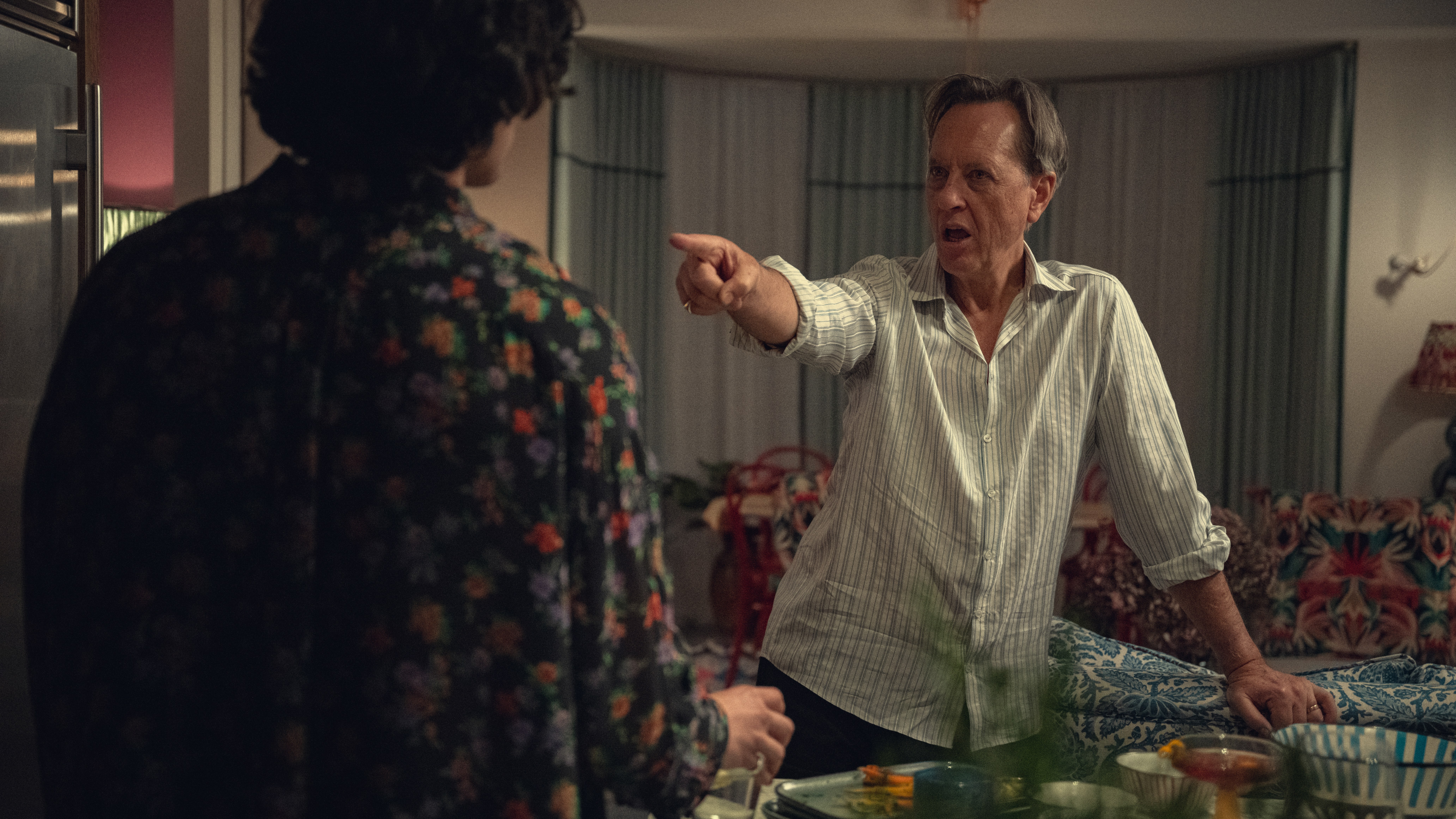 richard e grant as jonno pointing a finger in a living room in too much