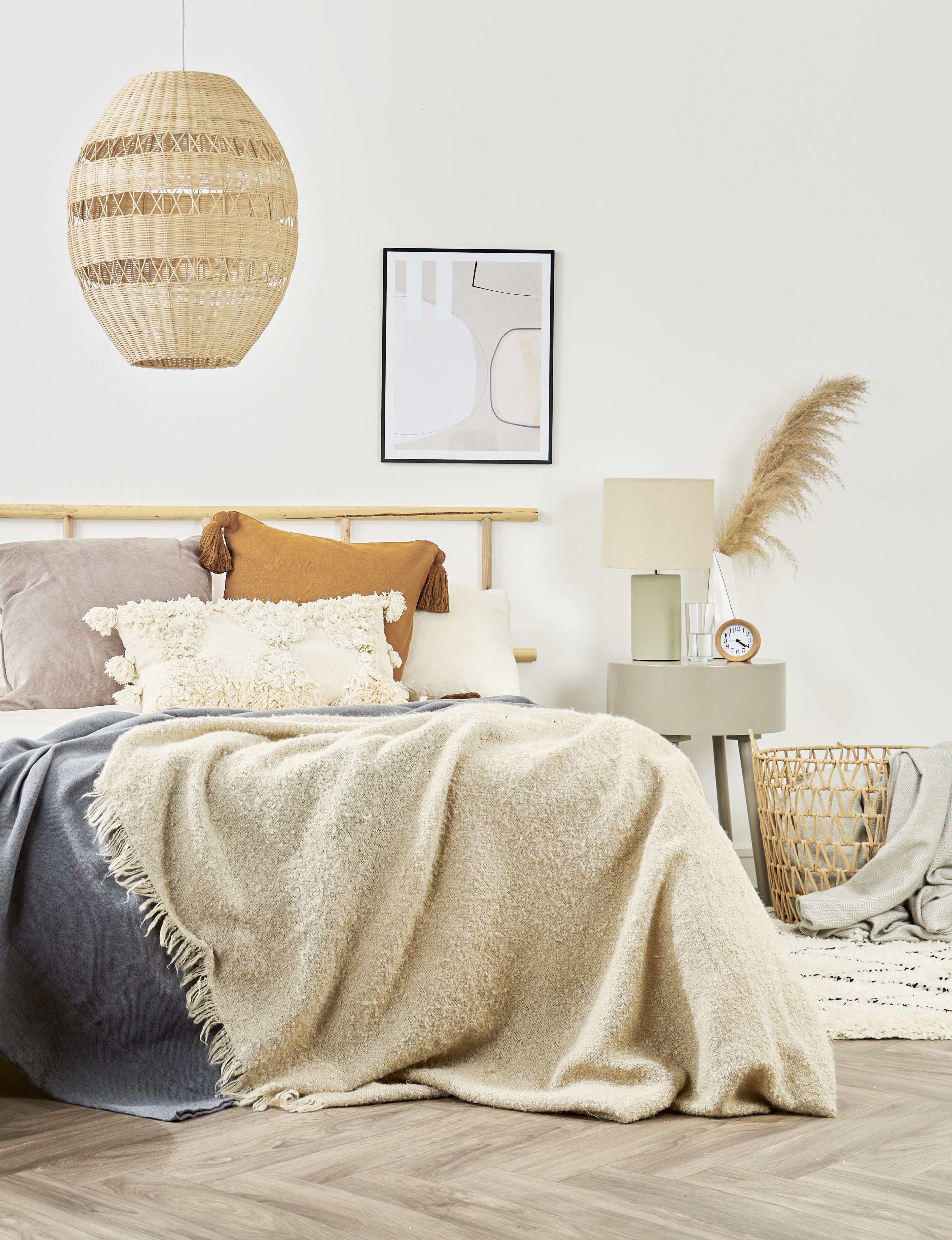 neutral boho style bedroom with large rattan pendant, textured blankets, rattan bin