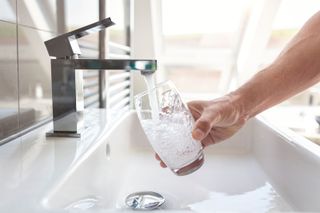 A person filling a glass with water from a chrome kitchen mixer tap