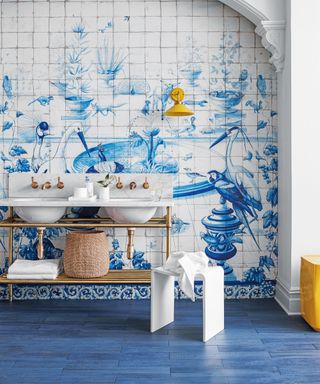 Blue bathroom with tile mural, blue flooring, yellow accents, twin sink in white and metal