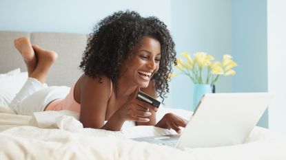Black woman in bed shopping online with credit card