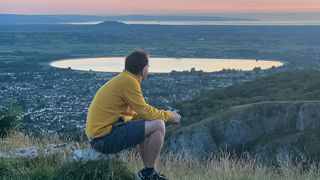 A picture of a man on top of a cliff watching as the sun sets in the distance