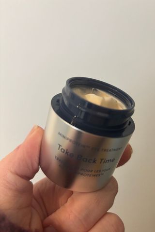 a hand holding a tub of trinny take back time cream