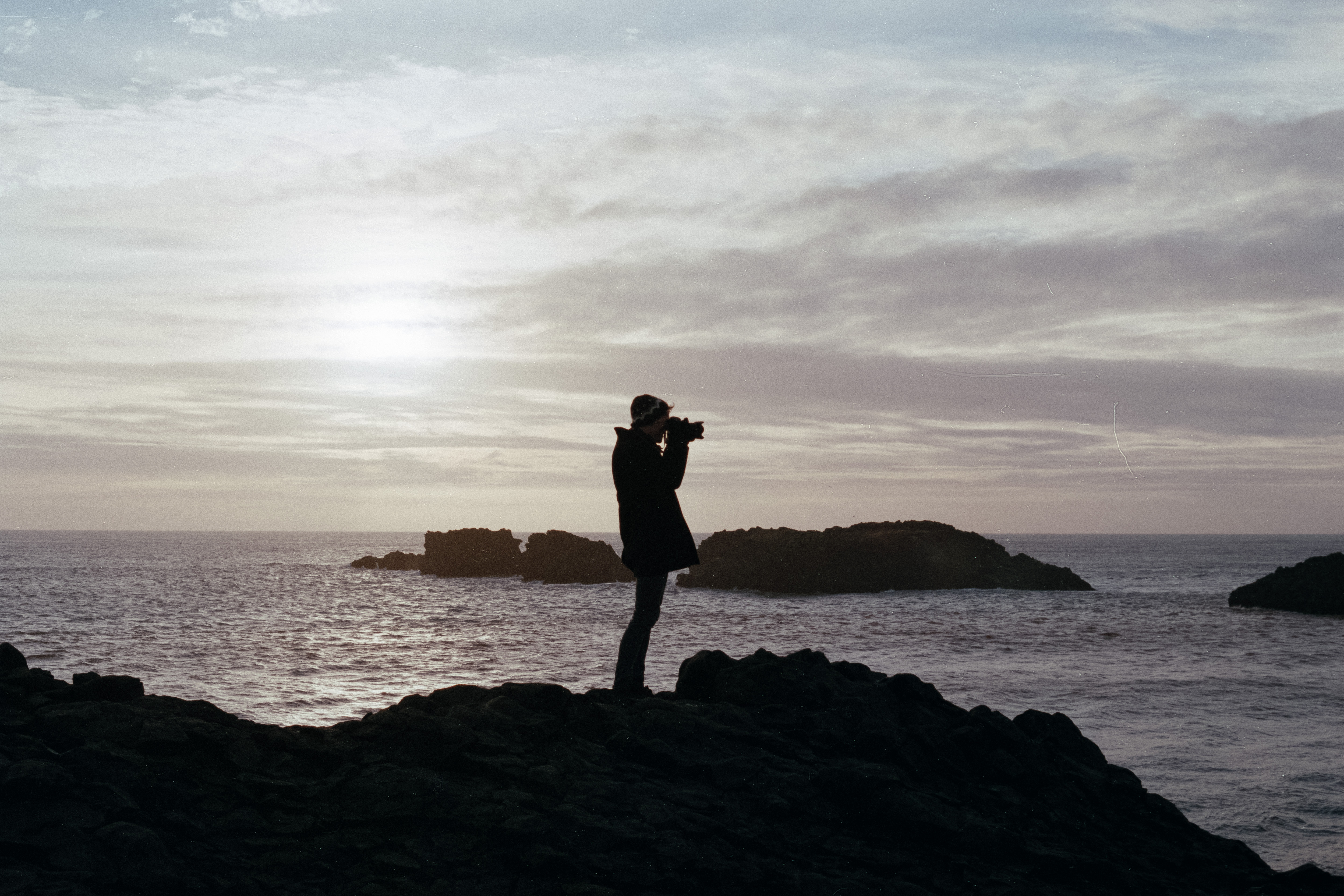 Person standing on the edge of a cliff overlooking the sea taking a photo