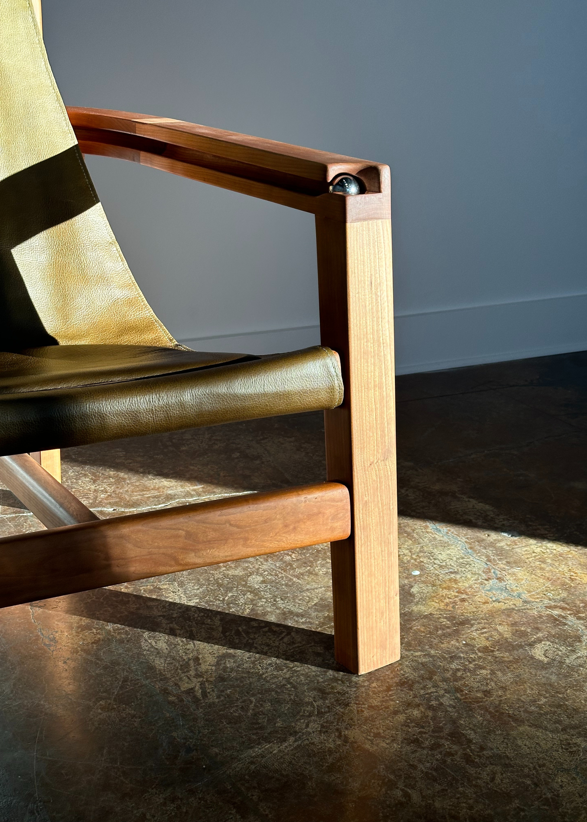 A corner of a wood chair with a metal ball and a green leather-like seat