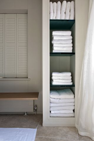 Open cupboard with selves for towels and a bench with a radiator underneath it
