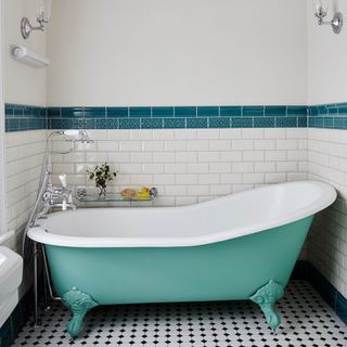 bathroom with roll top bath in green tiled white walls with a darker green stripe and black and white tiled flooring