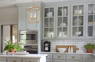 A white, tiled kitchen with eggshell colored, glass front cabinetry