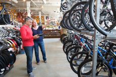 A salesperson is pointing to bikes on two levels to a customer in a bike shop
