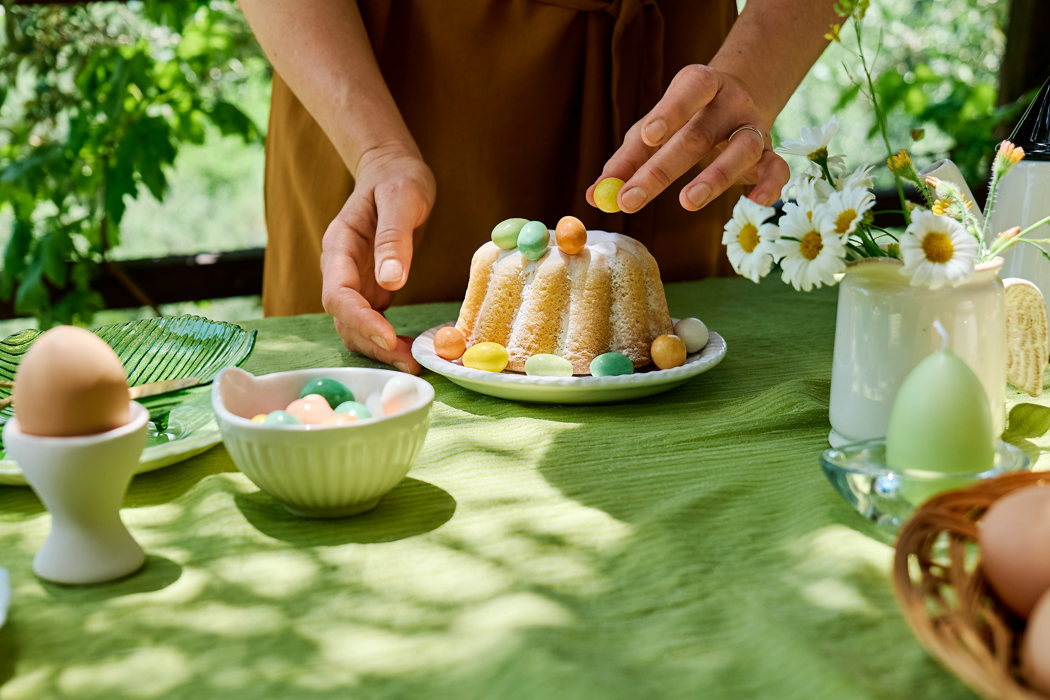 A person adding the finishing touches to their Easter baked goods on a green table cloth.