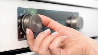 Woman adjusting modern white oven in kitchen.