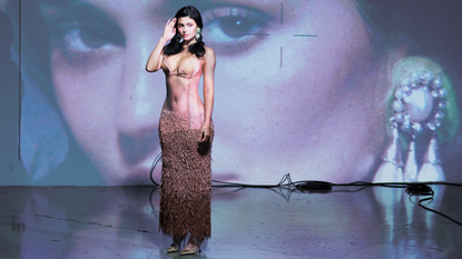 Kylie Jenner photographed by Aidan Zamiri for Who What Wear. She is standing in front of a projected image of herself wearing a Schiaparelli look. 
