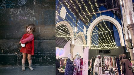 A composite image features two distinct scenes side-by-side: On the left, a small child, wearing a red dress and grey socks and shoes, stands against a dark wall covered in white chalk graffiti (including the word "TOAD" and "FRED"). The child is looking to the left with their mouth open and tongue slightly out, holding a small white object. On the right, the interior of a large hall, decorated with warm white string lights draped across the high, exposed wooden ceiling and large white stone arches, hosts a clothing bazaar with vendors and people browsing racks of clothes.