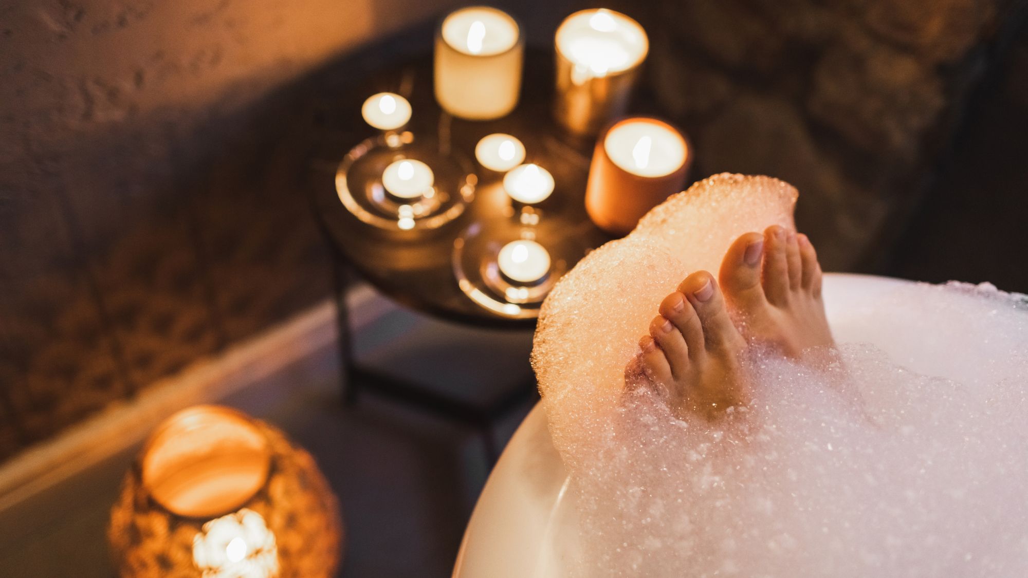 woman in a bath with her toes peeping out the bottom with candles in the background - best bath products