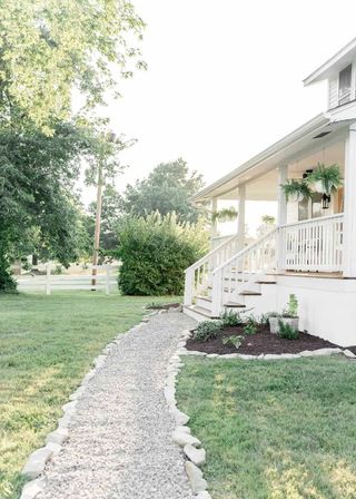 Gravel front yard walkway ideas surrounded by lawn, leading to a white painted porch.