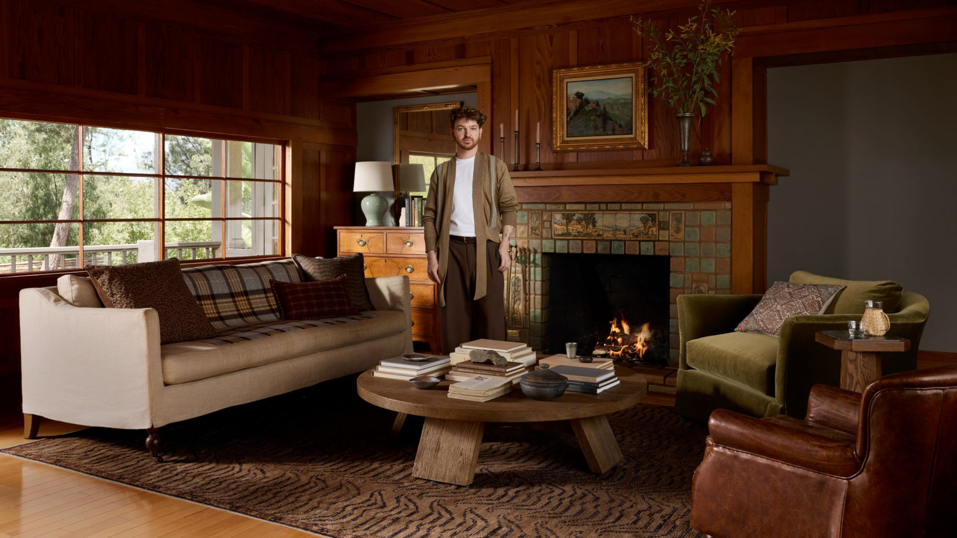 a cozy living room with a tan sofa, a wooden coffee table, wood-paneled walls, and a man standing in the center