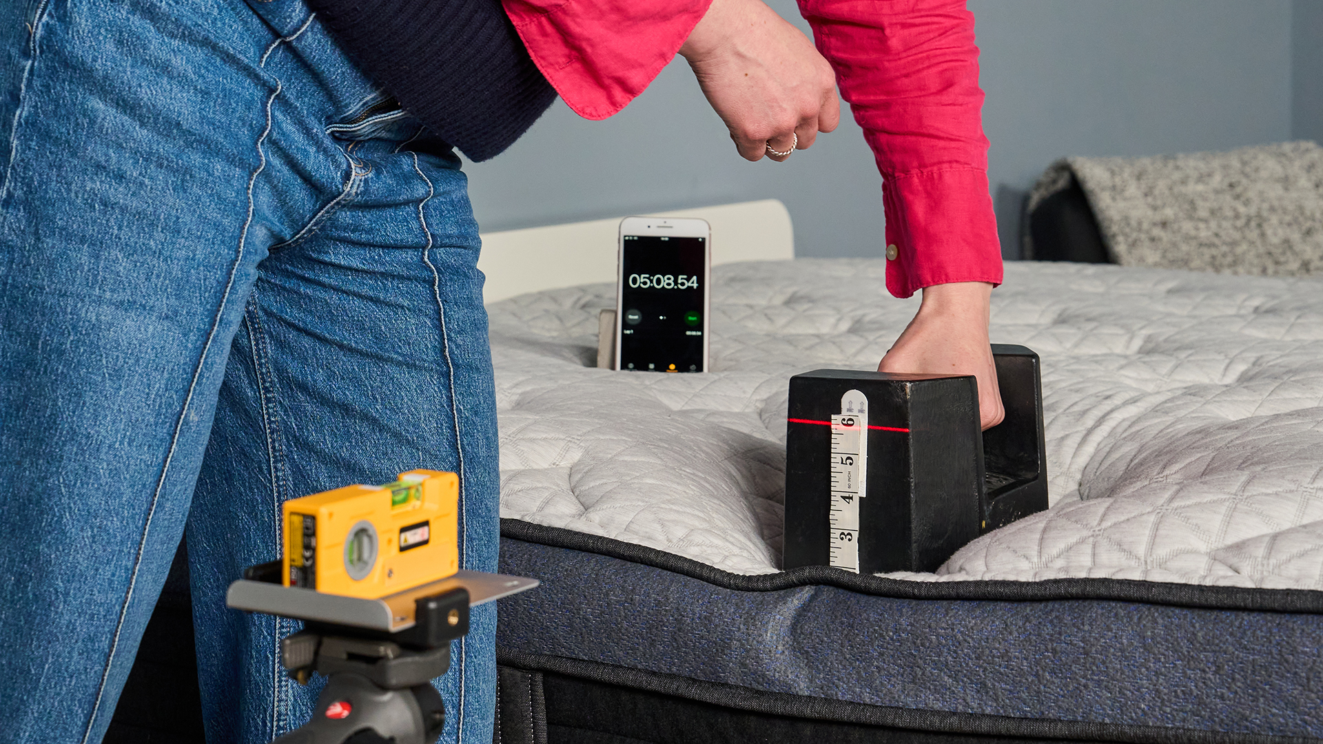 A close up of Nicola Appleton removing a 25kg weight from the edge of the Helix Midnight Luxe mattress after it has sat there for 5 minutes. A laser is pointed at the side of the weight, where a tape measure is placed