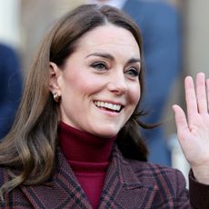 Kate Middleton wearing a plaid coat and red turtleneck waving 