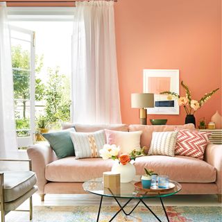 Living room with pink walls, white floor and curtains, French windows open to the garden, and furniture and decorations in pastel blues, pinks, and yellows
