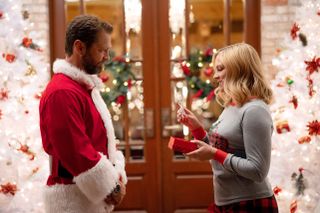 Jason Priestly and Melissa Joan Hart stand in front of a Christmassy door and exchange gifts