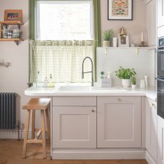 Kitchen with white painted walls, light pink kitchen cupboards and a kitchen sink with grey gingham curtains above it