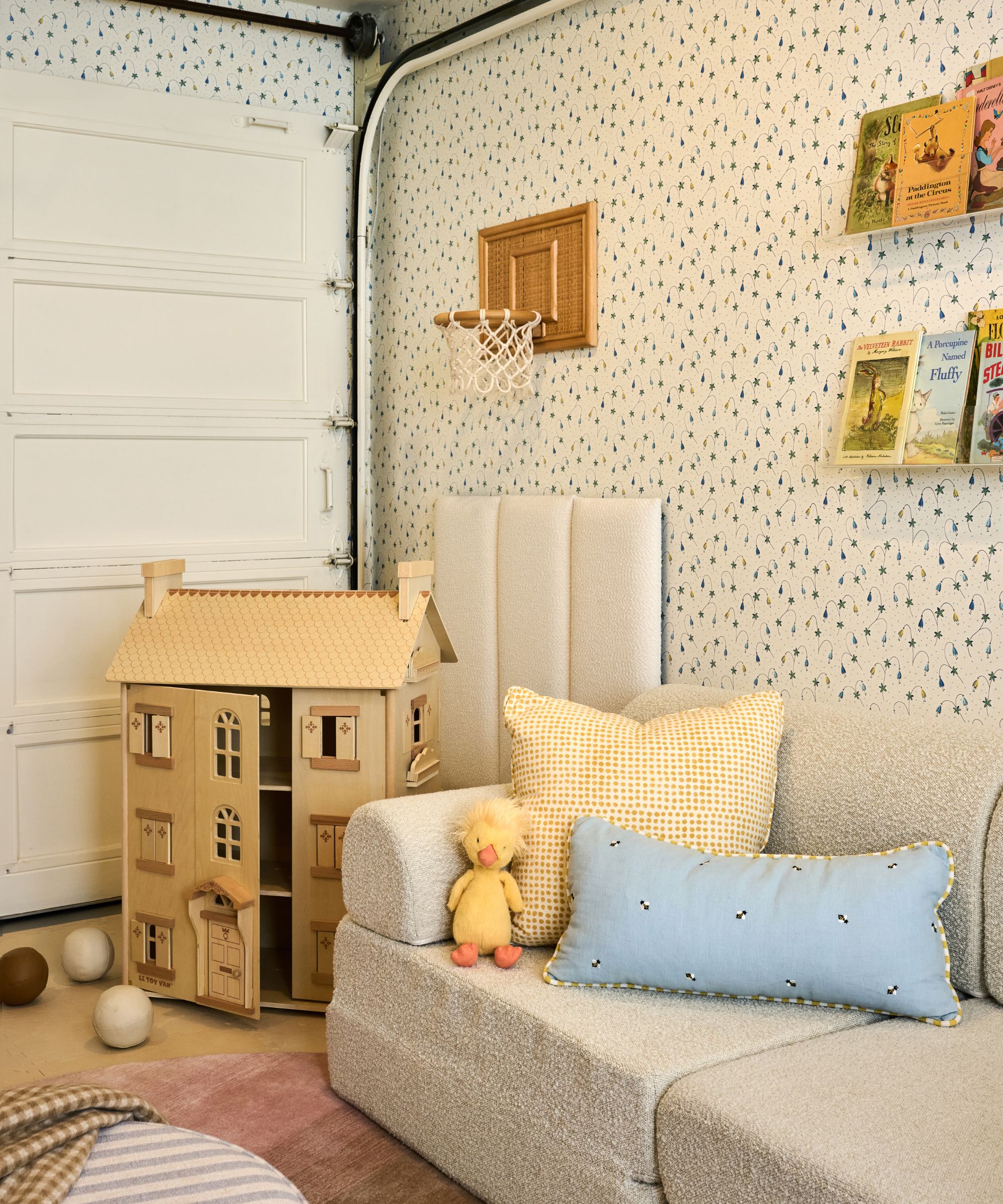 a floral wallpapered garage converted into a charming playroom with sofa, dolls house and book shelves