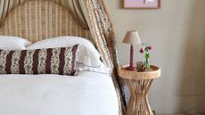 Textured lampshade set on an lacquered oxblood base perched atop of a sculptural natural fiber side table inside of a neutrally patterned bedroom