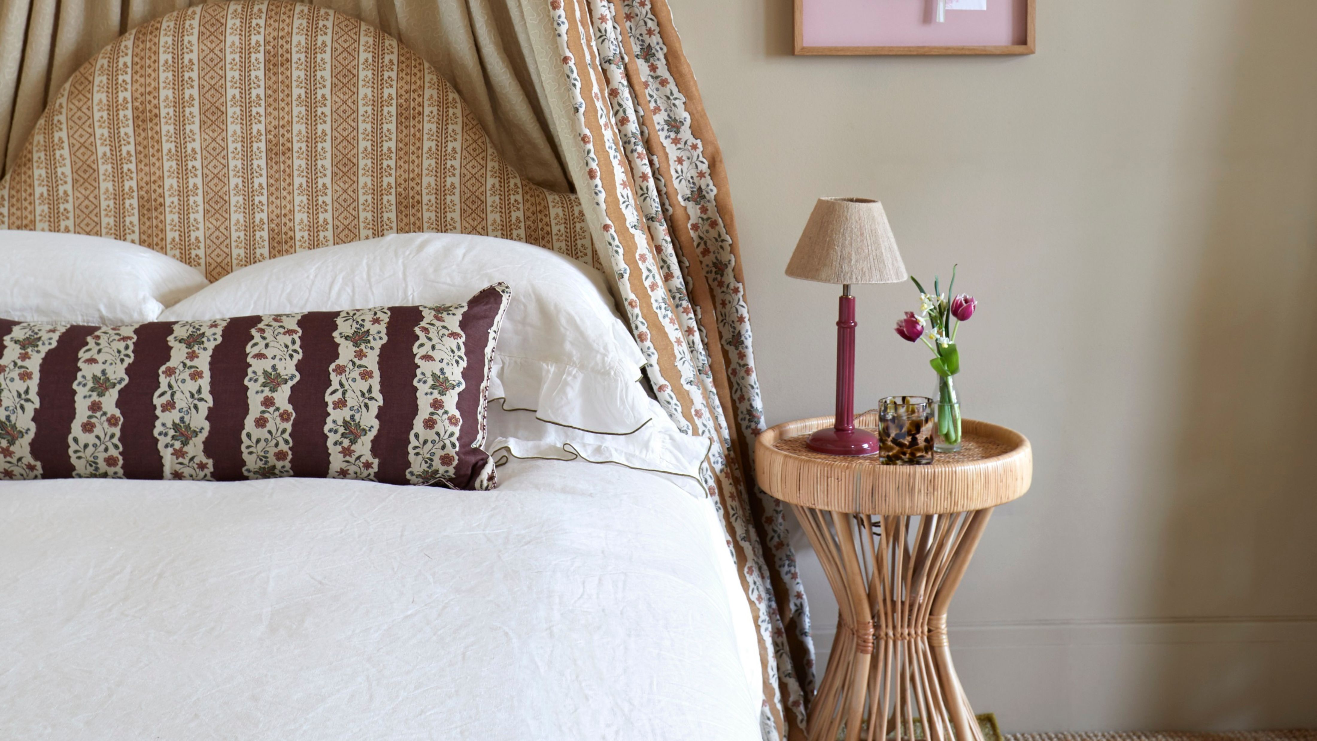 Textured lampshade set on an lacquered oxblood base perched atop of a sculptural natural fiber side table inside of a neutrally patterned bedroom