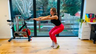 Woman with her heels raised on a dumbbell squats holding her arms out in front of her