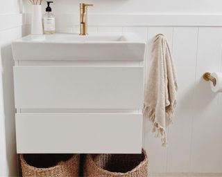 a white bathroom vanity with decorative storage underneath with baskets and a handtowel