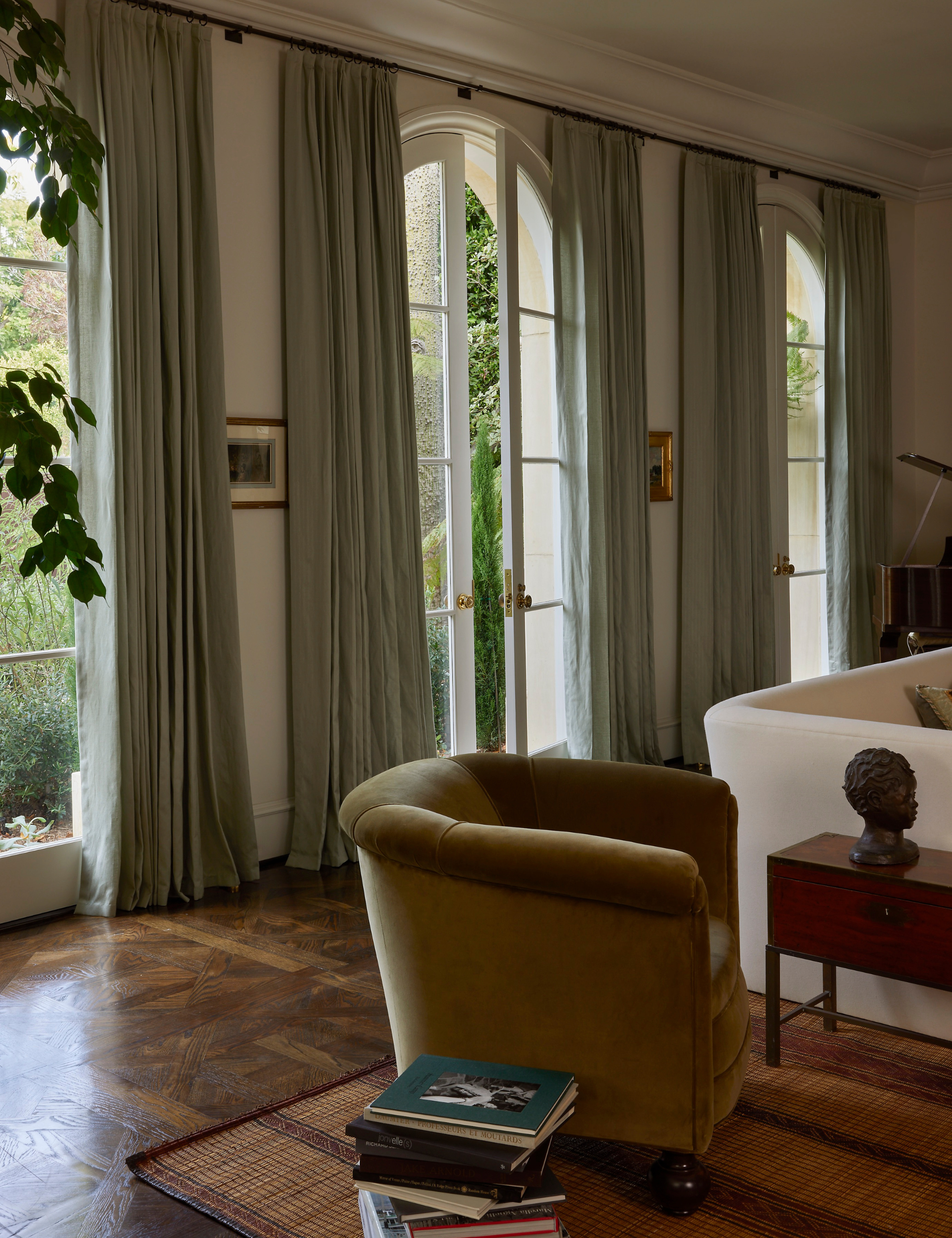 Warmly layered living room featuring a sculptural velvet armchair, a stack of books, and blue curtain panels.