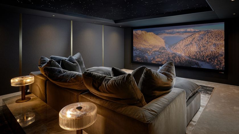 A photograph of a luxury, custom-installed home cinema with a huge projector screen, lush u-shaped sofa, grey walls and lamps