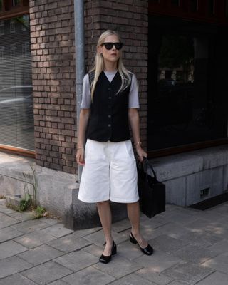 Linda Tol wearing a black vest and longline white shorts.