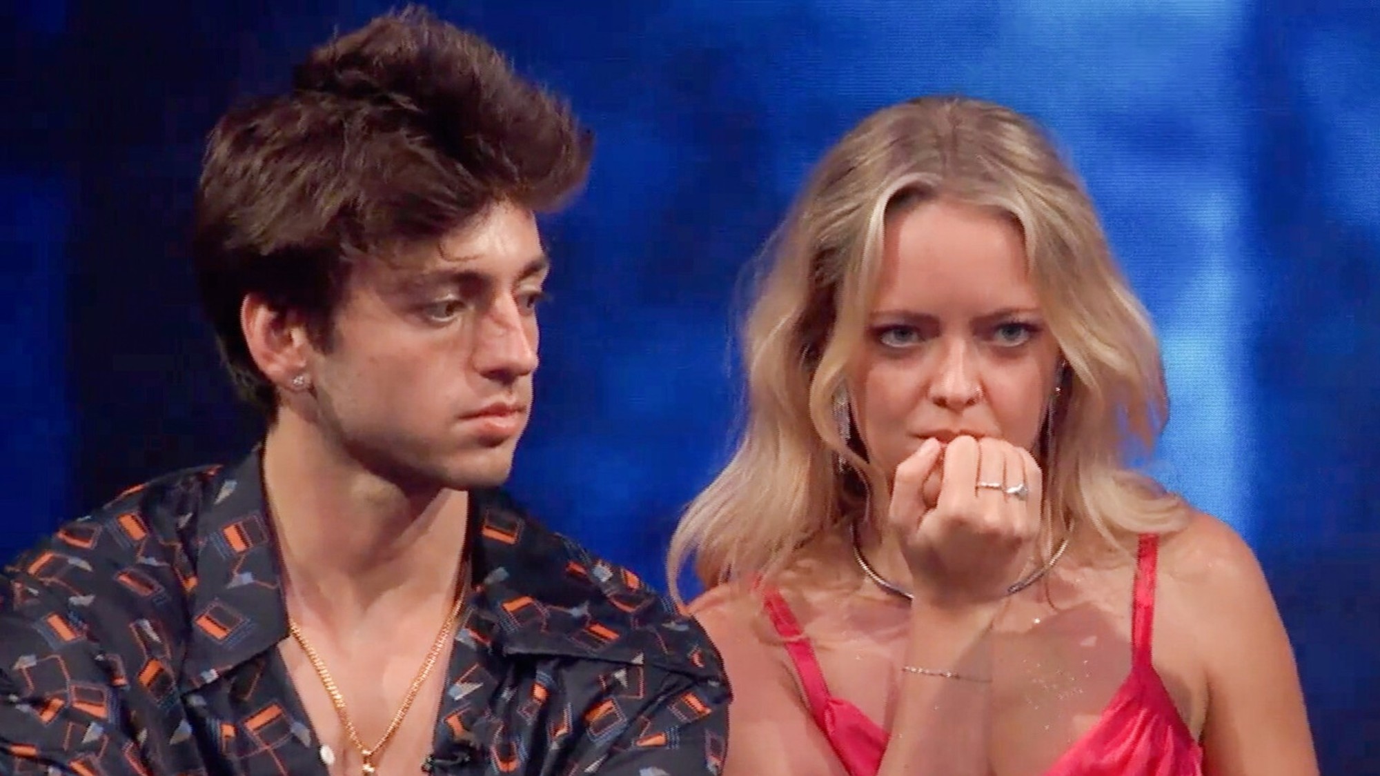 Drew and Melody during the Disco competition in Big Brother Season 28. He's wearing a colorful shirt with an open chested look. She's wearing a pink top and is biting her nails. 