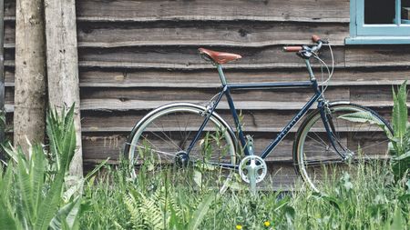 A dark navy Pashley bike with brown leather seat and handles leaning against a wooden shed