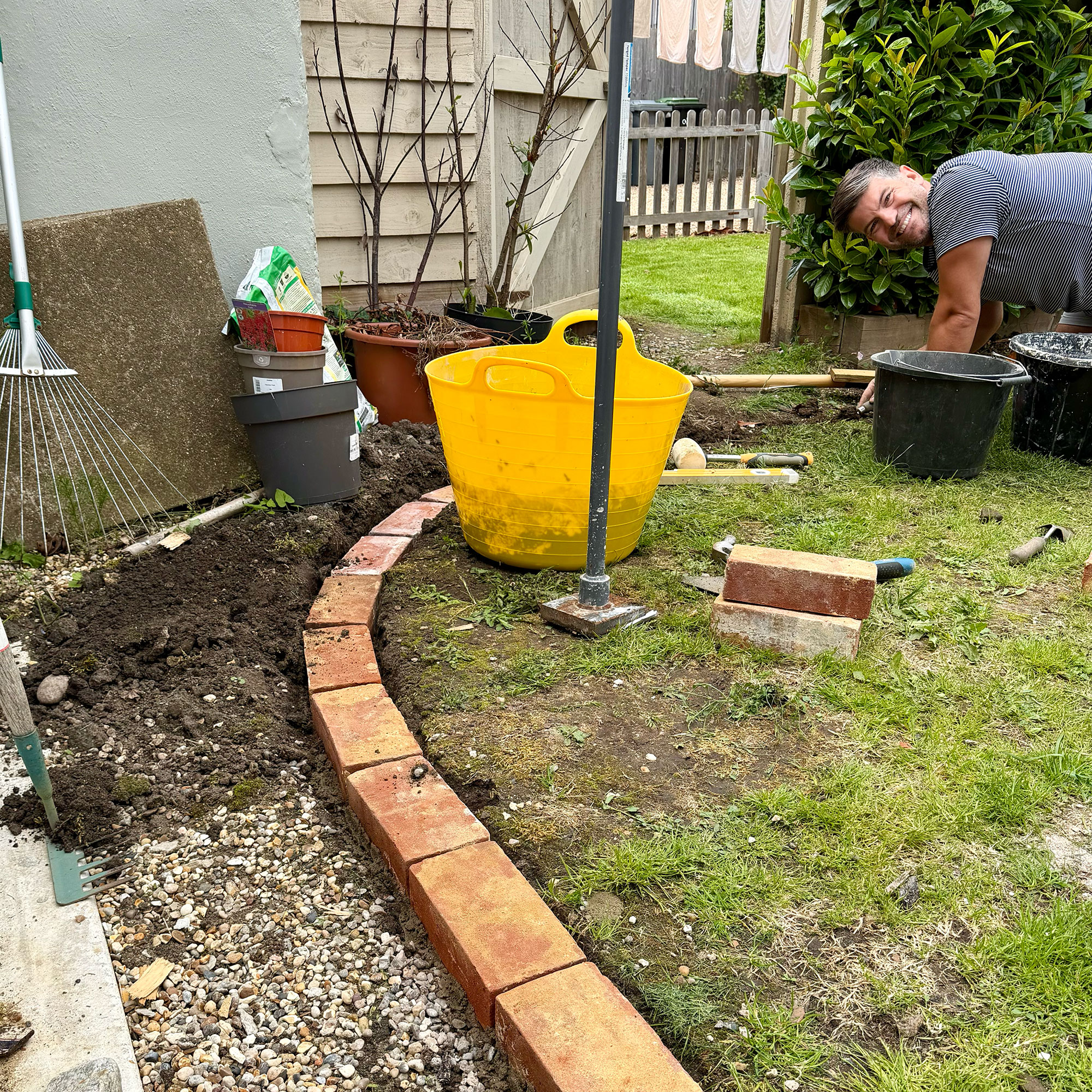 Man laying border of bricks around grass in garden
