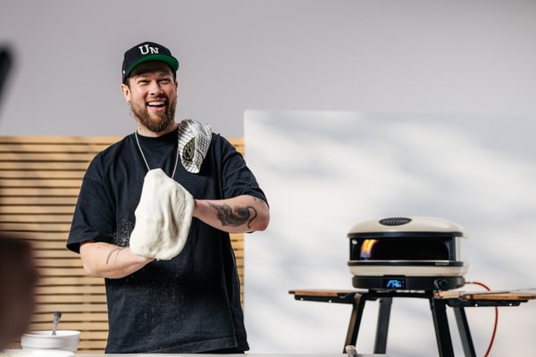 Tom Gozney spinning pizza dough beside Gozney pizza oven