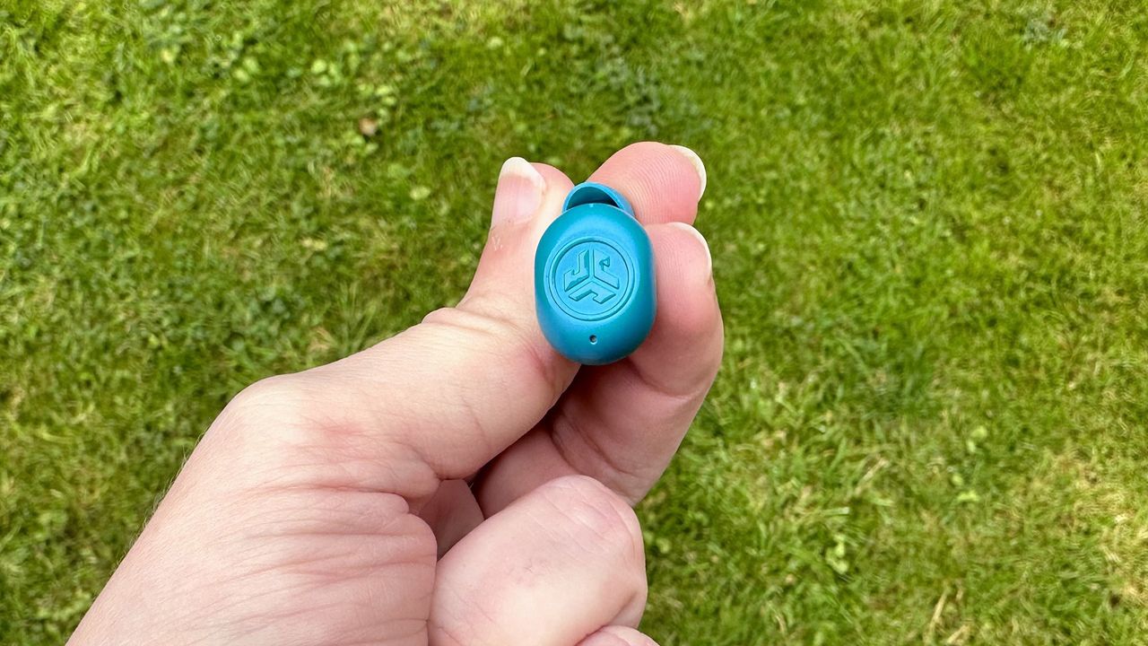 A hand holds one of the JLab JBuds Mini in their hand