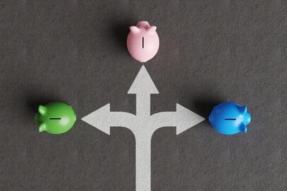 White divided road sign mark on asphalt with 3 different colored piggy banks going to different directions. Illustration of the concept of stock picks and varied investment products