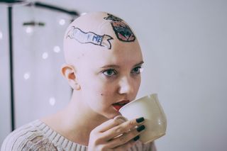 Nikki Black with bald tattooed head sipping from a cup