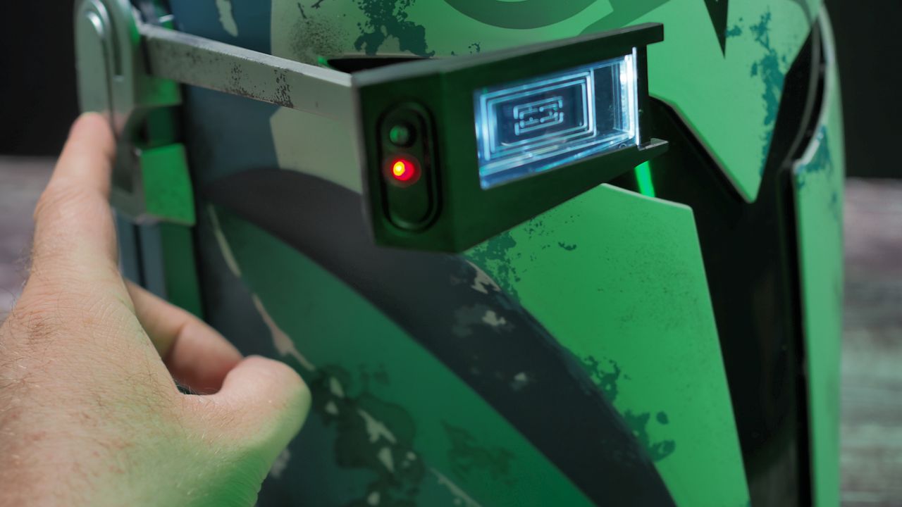 A closeup view of The Black Series Bo-Katan helmet rangefinder, with a hand pressing the button that lowers it