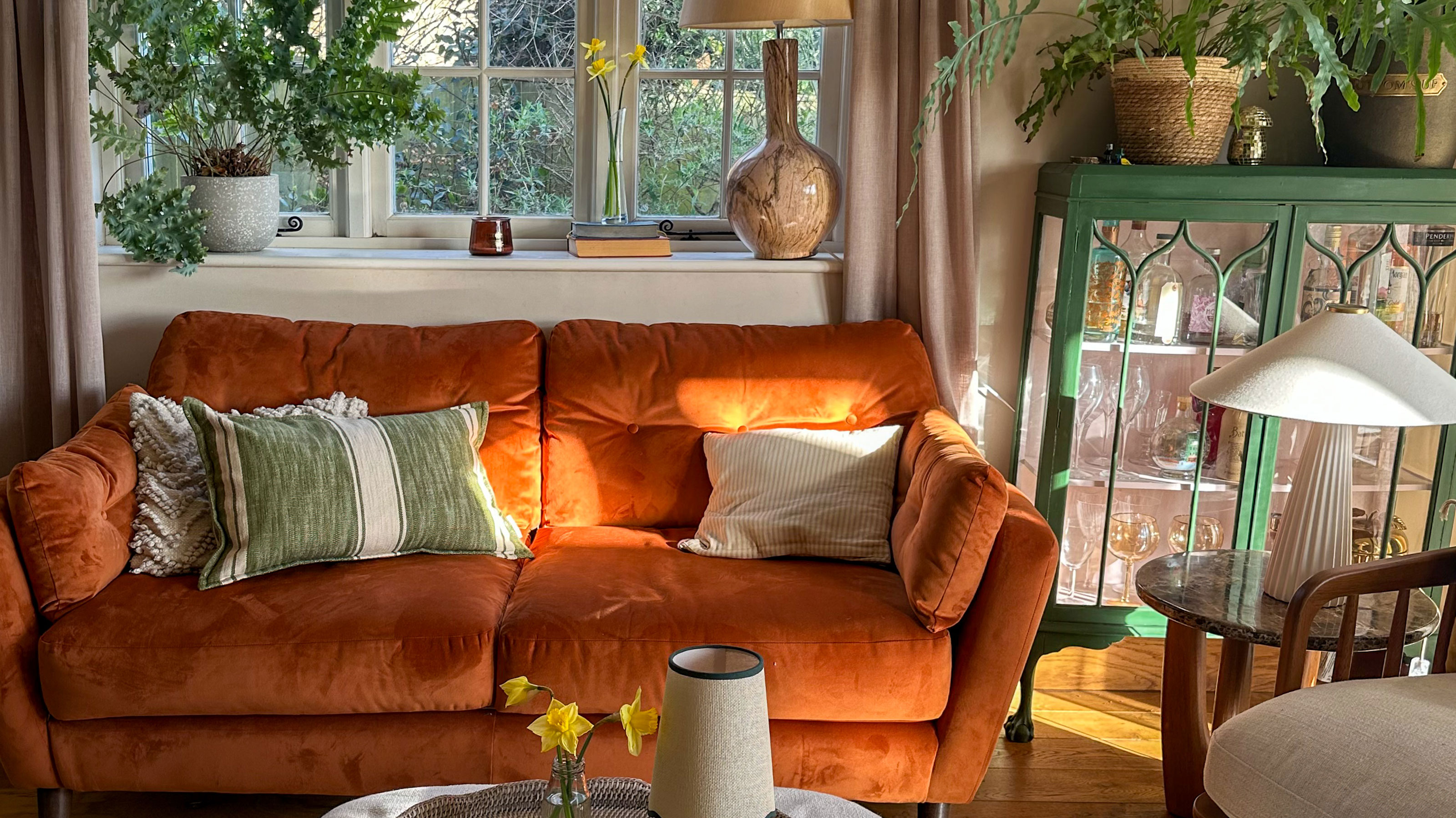 Living room with orange sofa, green cabinet bar cart and round wooden side table with lamp